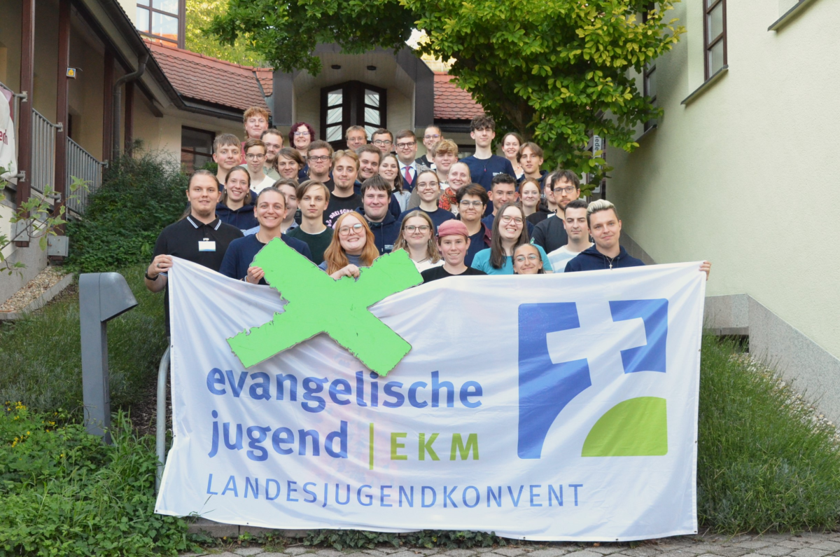 Gruppenfoto LJKHerbstVV2025 Gruppenfoto von etwa 35 jungen Erwachsenen und Jugendlichen, die eng zusammenstehen und fröhlich in die Kamera lächeln. Vorne halten mehrere Personen ein großes Banner mit der Aufschrift ‚evangelische jugend | EKM Landesjugendkonvent‘. © ekmjugend Gruppenfoto LJKHerbstVV2025 Gruppenfoto von etwa 35 jungen Erwachsenen und Jugendlichen, die eng zusammenstehen und fröhlich in die Kamera lächeln. Vorne halten mehrere Personen ein großes Banner mit der Aufschrift ‚evangelische jugend | EKM Landesjugendkonvent‘. © ekmjugend